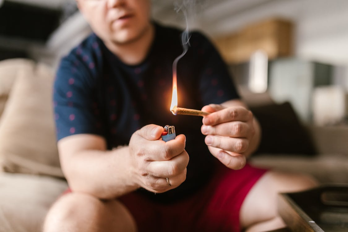 a man sitting on a couch, lighting a joint.