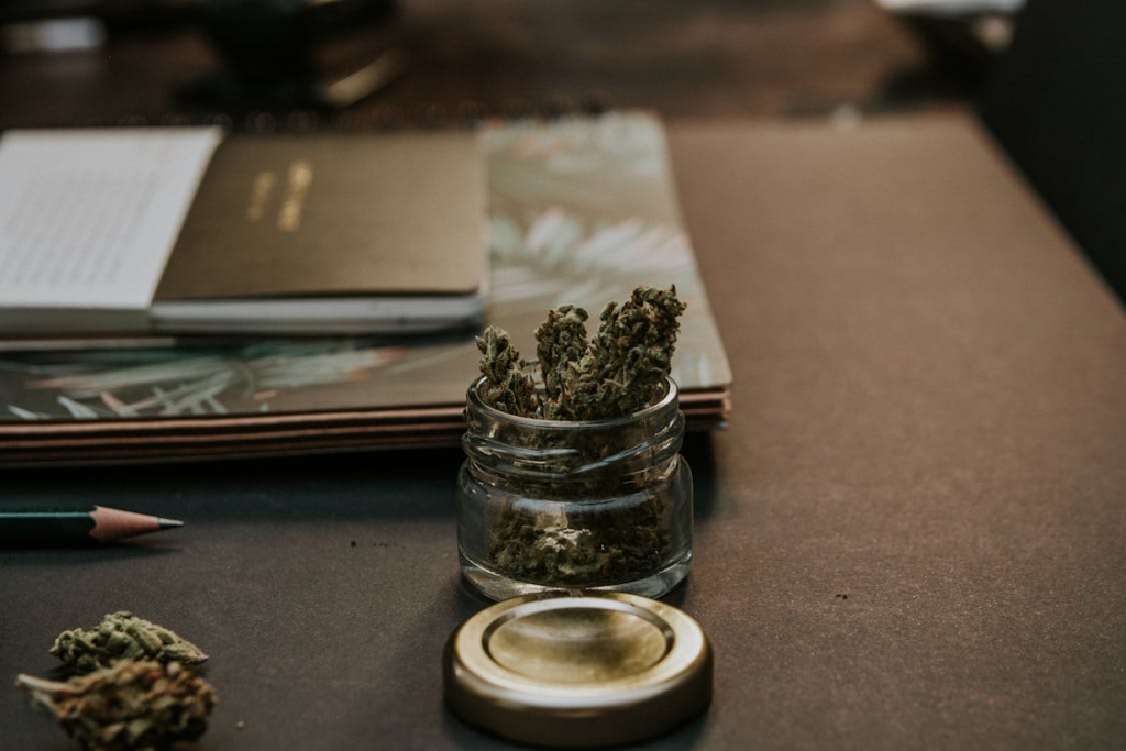 Small glass jar holding cannabis flower on a desk, representing an introduction to cannabis basics for beginners exploring strains and products.