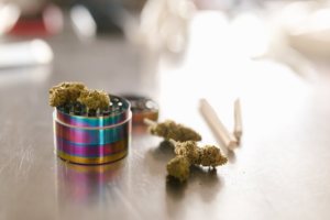 Close-up of colorful metal grinder with cannabis flower and pre-rolls on a reflective surface representing must-have cannabis accessories