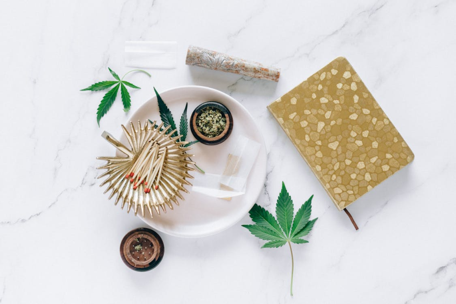 An image of a brown notebook beside a ceramic white plate and small cannabis flowers