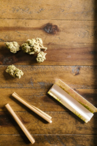 An image of rolled paper and cannabis flowers on a wooden surface